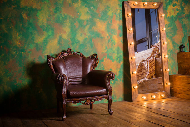 Μια όμορφη vintage δερμάτινη πολυθρόνα με ξύλινες λεπτομέρειες σε πράσινο φόντο τοίχου - Φωτογραφία, εικόνα