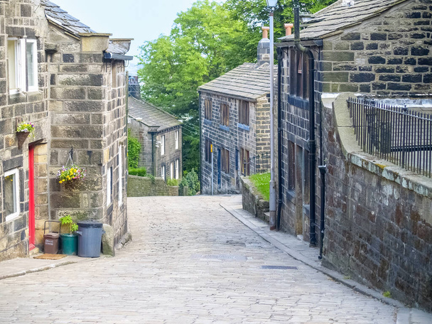 Небольшая английская традиционная деревенская дорога, ведущая вниз между каменными зданиями. - Фото, изображение
