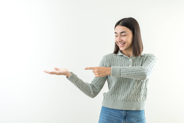 Menina feliz oferecendo e apresentando um produto ou mensagem sobre a mão em espaço vazio cópia. Com cabelo curto camisola verde e jeans. Olhando para a câmera - Foto, Imagem