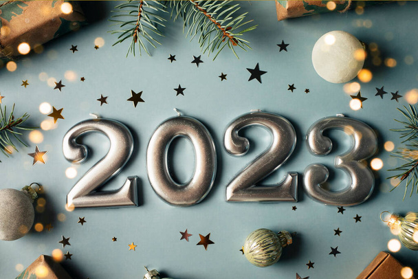 Liczby roku 2023 robione przez swiece. Drzewo jodłowe, pudełko prezentów, świąteczne dekoracje na niebieskim tle. Świąteczna pocztówka. Szczęśliwego Nowego Roku 2023 koncepcja karty. Płaskie ułożenie, widok z góry. - Zdjęcie, obraz