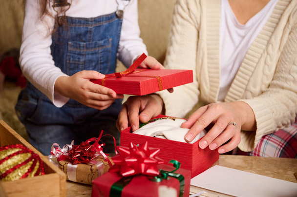 Мать и дочь крупным планом упаковывают подарки на Рождество или Новый год, с нетерпением ожидая предстоящих зимних праздников. Счастливые семейные отношения. Волшебная праздничная атмосфера в уютном интерьере дома - Фото, изображение