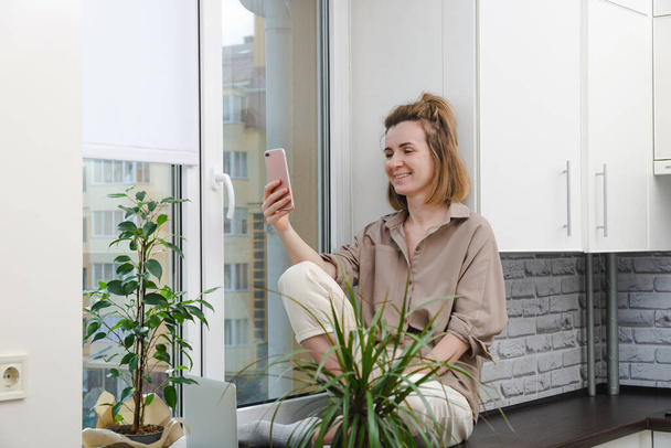 Žena se usmívá dělat video hovor doma oknem. - Fotografie, Obrázek