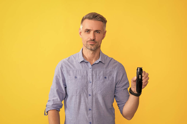 чоловік тримає електричну бритву на жовтому фоні, гоління
. - Фото, зображення