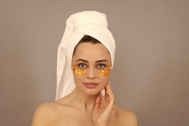 aistillinen nainen froteepyyhkeellä käyttää kasvojen kultainen silmälappu iholle, kylpylä. - Valokuva, kuva