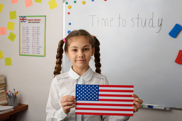 Niña con bandera de los EEUU en la lección de País estudiando contando sobre los EEUU a los compañeros de clase. Niños preparados contando historias sobre los Estados Unidos de América, llevando a cabo su tarea en casa - Foto, imagen