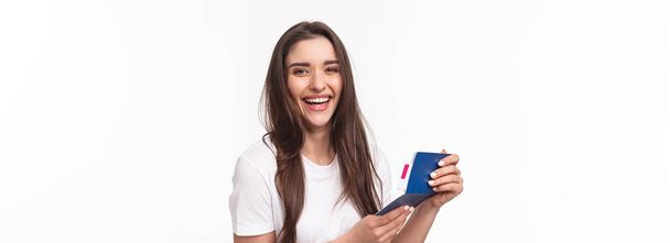 Travelling, holidays, summer concept. Close-up portrait of happy, charismatic pretty woman laughing, looking at her visa in passport with plane ticket, smiling joyful camera, ready for journey. - 写真・画像