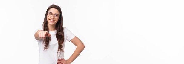 Waist-up portrait of happy smiling young woman inviting you join her team, recruit person, pointing finger at camera grinning and standing confident in her choice, white background. - Photo, Image