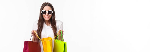 Shopping, leisure and lifestyle concept. Portrait of excited happy young girl likes shop, attend favorite mall, got lots of new clothes, bragging it, open up bag to show friend, smiling enthusiastic. - Photo, Image