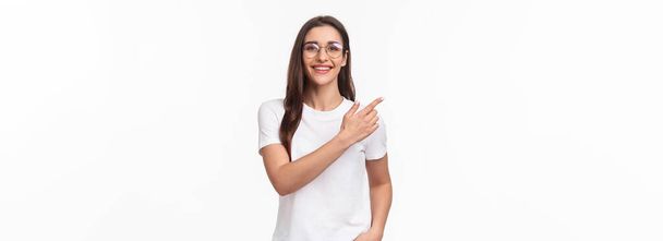 Waist-up portrait of friendly, attractive young 20s woman in glasses, giving advice, recommend try this online shop, click link or visit promo page, pointing finger upper left corner, smile camera. - Photo, image