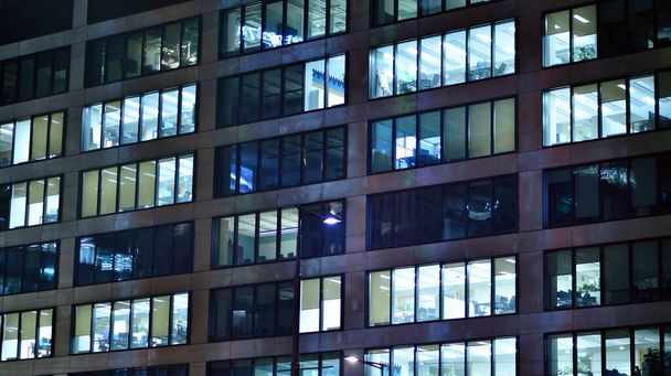 Modern irodaház a városban éjszaka. Kilátás egy vállalati épület megvilágított irodáira. Villogó fény a többszintes üveg- és acélépület ablakában. Hosszú expozíció éjszaka - Fotó, kép