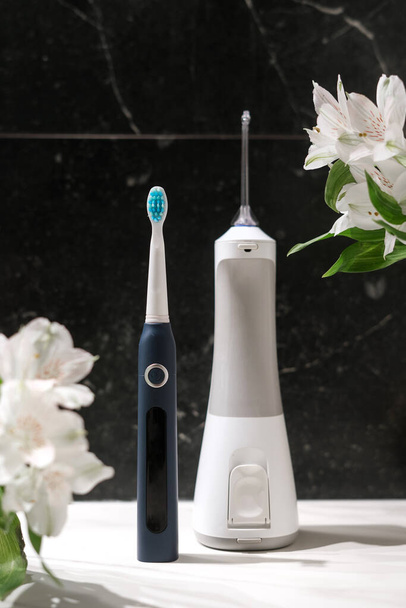 dental health care products, sensitive teeth brush and electric irrigator for daily individual usage and lilies flowers on dark marble background - Photo, Image