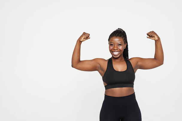 Young black sportswoman with afro pigtails showing her biceps isolated over white background - Foto, imagen