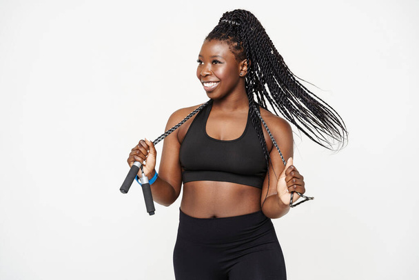 Black young sportswoman smiling while posing with jumping rope isolated over white background - Foto, Imagen