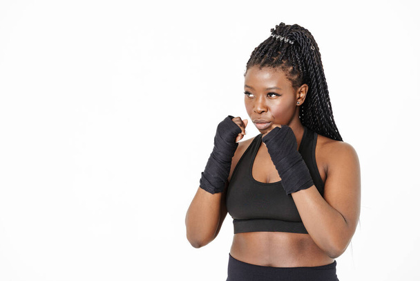 Μαύρη νεαρή γυναίκα κοιτάζει στην άκρη, ενώ ποζάρουν σε επίδεσμο πυγμαχίας απομονώνονται σε λευκό φόντο - Φωτογραφία, εικόνα