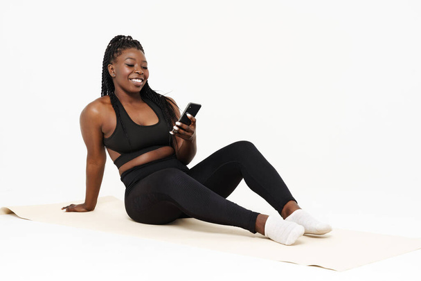 Black young woman using cellphone during yoga practice isolated over white background - Фото, зображення