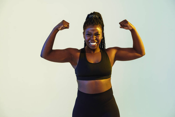 Black young sportswoman grimacing while showing her biceps isolated over white background - Foto, Bild