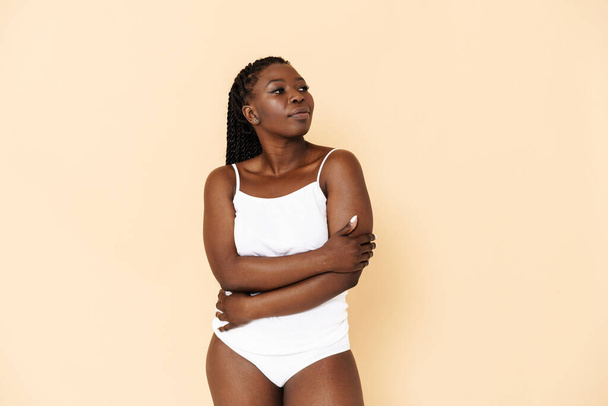 Black young woman with afro pigtails posing in underwear isolated over beige background - 写真・画像