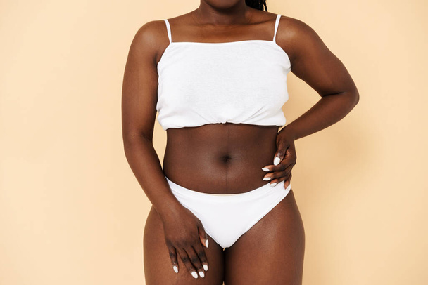 Black young woman posing in white underwear isolated over beige background - Fotografie, Obrázek