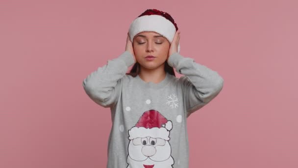 聞き耳を立てたくない。いらいらする若いクリスマスの女性は耳をカバーし、不快な騒音の声を無視する助言を避けるために、いいえジェスチャーをいらいらさせた。女の子オンスタジオピンクの背景 - 映像、動画