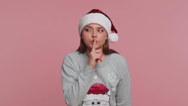 Cala-te, por favor. Retrato de mulher no Natal Santa Cláusula suéter velho pressiona dedo indicador aos lábios faz signo gesto silêncio não diz segredo. Jovem linda menina no fundo do estúdio rosa - Filmagem, Vídeo