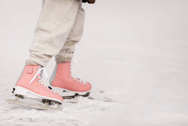 Foto recortada de las piernas de niña con patines rosados y ropa de abrigo en la pista de patinaje sobre hielo natural en el frío día de invierno. Patinaje sobre hielo infantil en el lago congelado con en el bosque nevado. Felices vacaciones - Foto, imagen