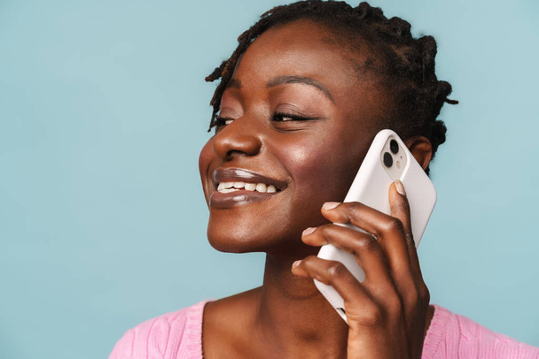 Afroamerykanka podekscytowana kobieta uśmiecha się podczas rozmowy przez telefon odizolowany na niebieskim tle - Zdjęcie, obraz