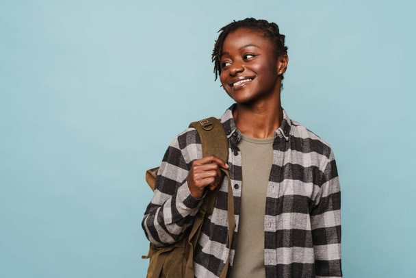African american young woman wearing plaid shirt and backpack smiling at camera isolated over blue background - Valokuva, kuva