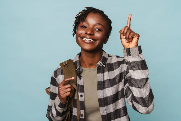 African american young woman wearing plaid shirt and backpack gesturing at copyspace isolated over blue background - Valokuva, kuva