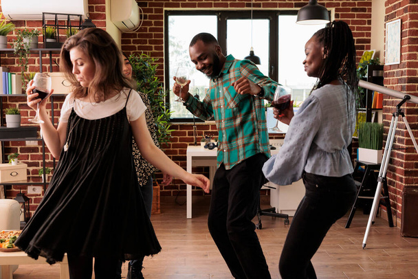 Various nationalities friends dancing. Diverse partners drinking wine, alcohol, having fun, enjoying social life, togetherness, friendship, partnership. Culturally distinct people chilling. - Foto, imagen