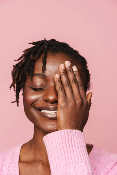 Black young woman with dreadlocks smiling and covering her eye isolated over pink background - Fotó, kép