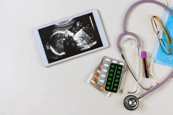 Tıp bürosundaki doktor, doğmamış çocuğun korunması için reçete yazan hamile kadının ultrasonunu inceliyor. - Fotoğraf, Görsel