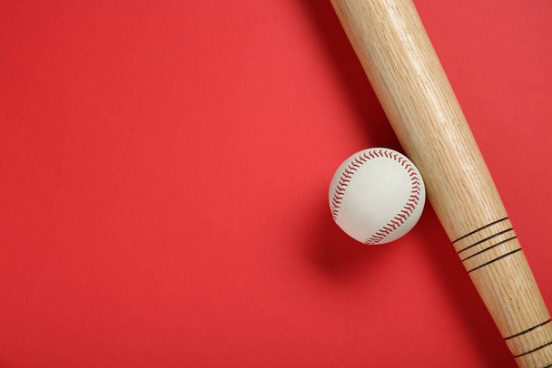 Bate y pelota de béisbol de madera sobre fondo rojo, plano. Espacio para texto - Foto, Imagen