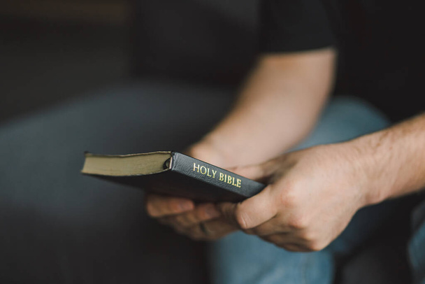 A keresztény ember a kezében tartja a szent bibliát. A Szent Bibliát olvasni egy otthonban. Fogalom a hit, a spiritualitás és a vallás. Béke, remény - Fotó, kép