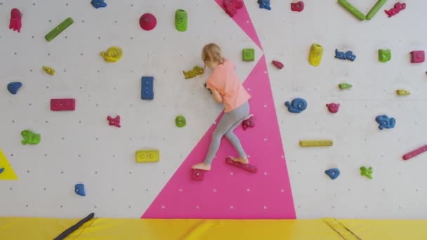 Brave bambino bambina bionda è arrampicata sulla parete artificiale in palestra di roccia esercizio. Infanzia e sport estremi concetto. - Filmati, video