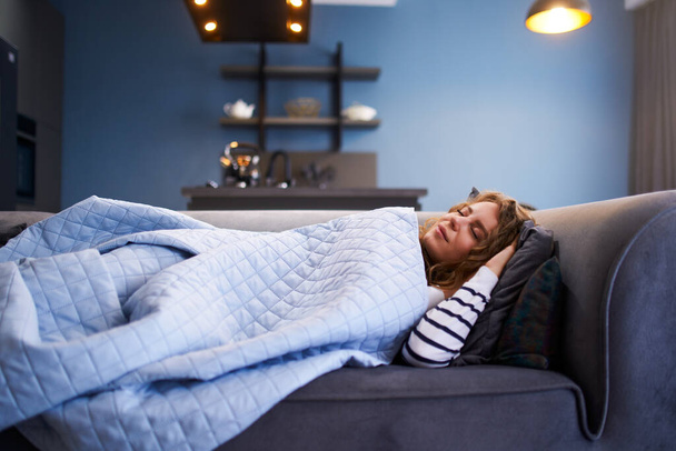 Girl sleeps on cozy sofa in living room at siesta time under warm blanket. Sleeping woman taking nap on the sofa during the day. - Фото, зображення