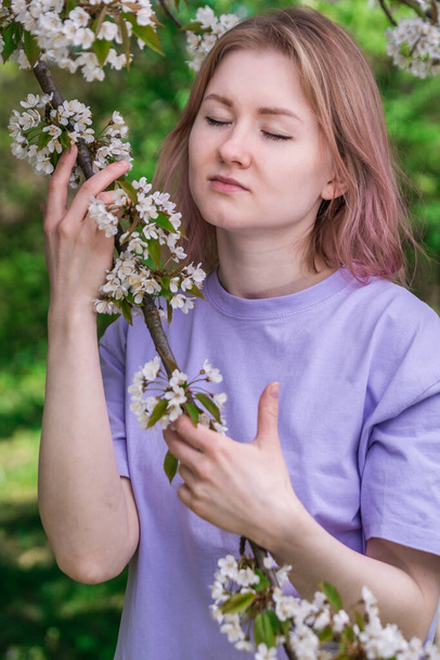 紫のTシャツにりんごの花を持った女性。りんご園の白い花の写真. - 写真・画像