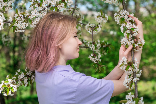 Feminino em uma camiseta roxa segurando flores de maçã. Foto macia com flores brancas no pomar da maçã. - Foto, Imagem