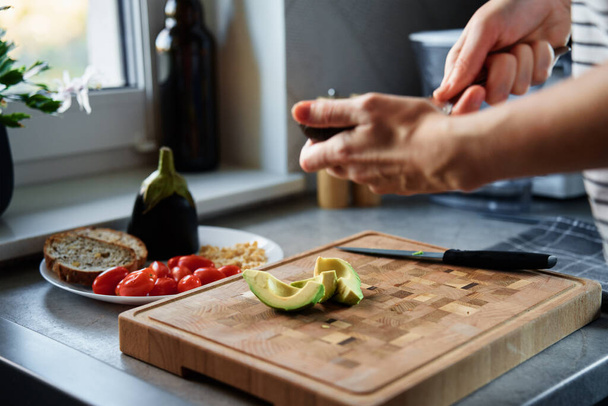 Proces van de vrouw snijden avocado voor toast in keuken interieur. Vrouw die 's morgens een gezond ontbijt bereidt. Veganistisch voedsel - Foto, afbeelding