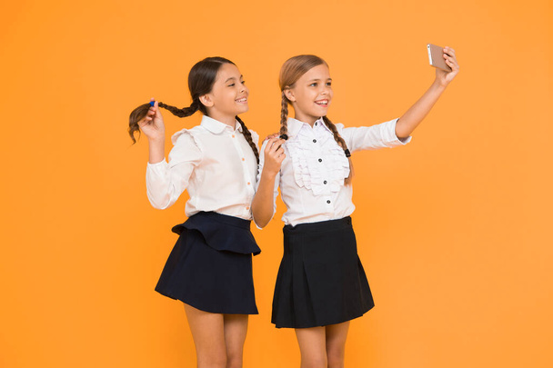 One more selfie. Happy schoolchildren taking selfie with smartphone on yellow background. Little girls smiling to selfie camera in mobile phone. Enjoying selfie session on september 1. - Valokuva, kuva