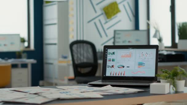 Порожній стартап-офіс з ноутбуком, що показує програмне забезпечення для ділових маніпуляцій на дисплеї, що показує рухомі діаграми та статистику на столі. Інтер'єр відділу маркетингу з портативним комп'ютером з erp
. - Кадри, відео