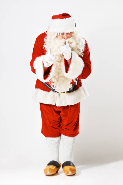 Christmas, santa claus and man in studio for secret, surprise and exciting good news against a white background mockup. Father christmas, costume and hand sign hush, quiet and festive celebration. - Photo, Image