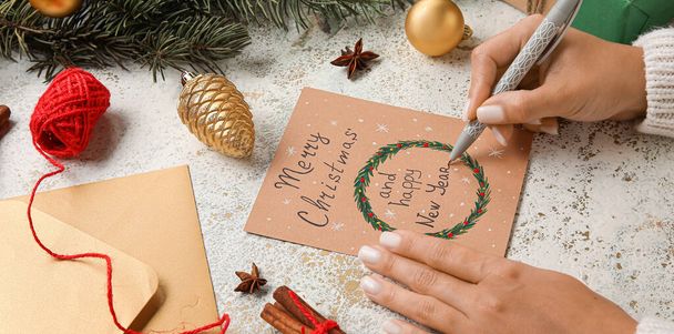 Frau mit Stift und Grußkarte für frohe Weihnachten und ein gutes neues Jahr am Tisch - Foto, Bild