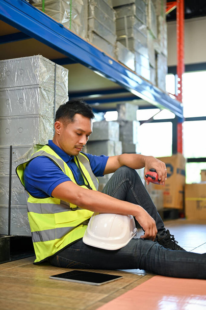 Portré, fáradt és feldúlt ázsiai férfi raktár dolgozó ül a raktárban. ipari, mérnöki, raktár vagy raktár munkások. - Fotó, kép