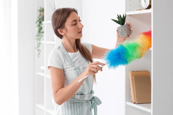 Young housewife cleaning shelf with duster at home - Foto, Bild