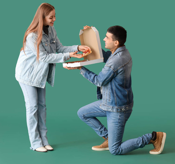 Happy young couple with fresh pizza on green background. Creative marriage proposal - Foto, imagen