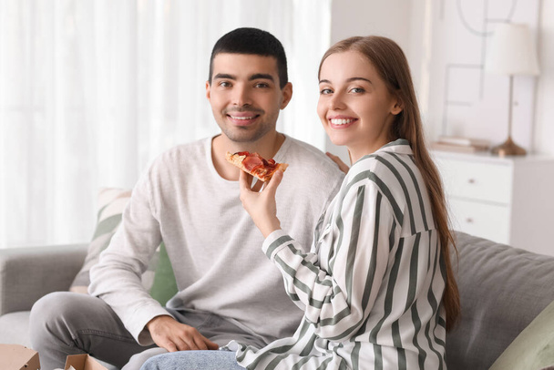 Happy young couple eating tasty pizza at home - Fotó, kép