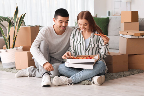 Happy young couple eating tasty pizza on moving day - Photo, Image