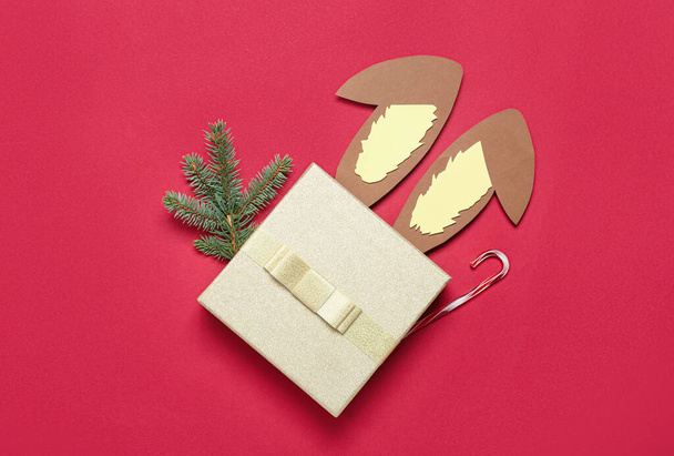 Orecchie di coniglio di carta con rami di Natale, regalo e canna da zucchero su sfondo rosso - Foto, immagini