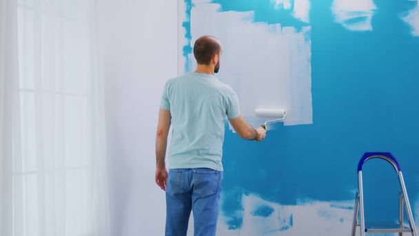 Cobertura de tinta azul de parede com tinta branca usando escova de rolo. Handyman a renovar. Apartamento redecoração e construção de casa, enquanto renovar e melhorar. Reparação e decoração
. - Foto, Imagem