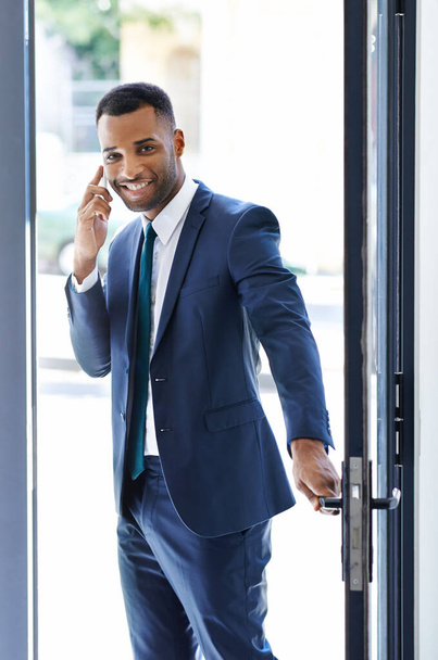 Entering the office with a smile. A handsome african american businessman using his smartphone while arriving at work - Photo, Image